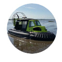 A lime green and black hovercraft with a large fan at the rear is partially submerged in shallow water under a blue sky.