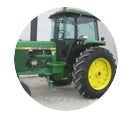 A partial view of a green and yellow John Deere tractor, seen from the side, enclosed within a white circular frame.